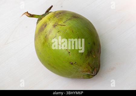 Fresh young green coconuts rest on a light wooden background. These coconuts haven't fully ripened and turned brown, offering sweet water and very ten Stock Photo