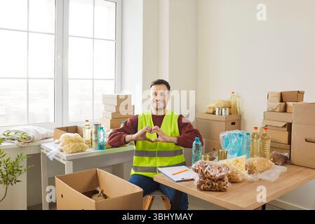 Young man volunteer making heart gesture by hands volunteering in charitable foundation. Stock Photo