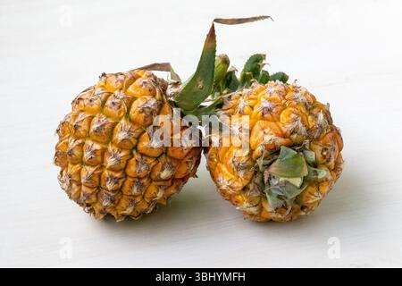 Two ripe pineapples (Ananas comosus) on light wood. Healthy fruit with vitamins, minerals, fiber, and antioxidants. Stock Photo