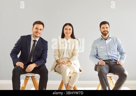 Smiling three diverse team posing differently looking at camera chair sitting, corporate staff Stock Photo