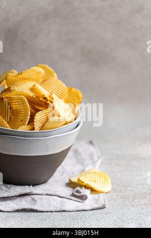 A bowl filled with golden homemade chips is set against a rustic background on a light fabric. The crispy texture and inviting presentation highlight Stock Photo