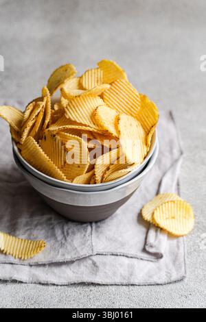 A bowl of crispy homemade potato chips served on a rustic fabric napkin. These golden, wavy chips offer a delicious, crunchy snack perfect for any occ Stock Photo