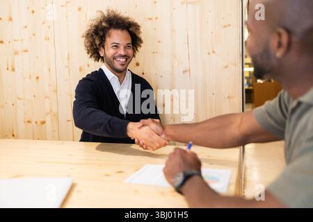 Professionals meet in a vibrant coworking space in Barcelona, shaking hands over a wooden desk, symbolizing collaboration and creativity in a modern o Stock Photo
