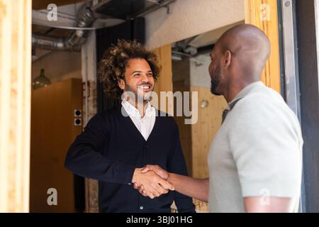 Two professionals exchanging a warm handshake in a vibrant coworking space in Barcelona, highlighting the collaborative spirit and networking opportun Stock Photo