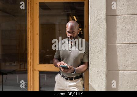 A business professional stands outside a coworking space in Barcelona, using a smartphone to connect and collaborate. The setting is vibrant and moder Stock Photo
