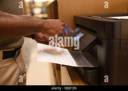 A man operates a printer in a modern coworking space in Barcelona, handling documents and charts. The image captures the collaborative working atmosph Stock Photo