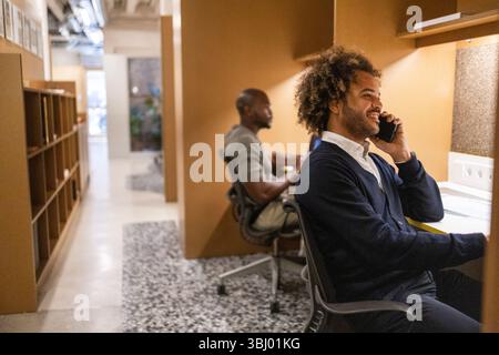 Two professionals engaged in work at a coworking space in Barcelona. One person is smiling on the phone, while another works on a laptop, creating a p Stock Photo