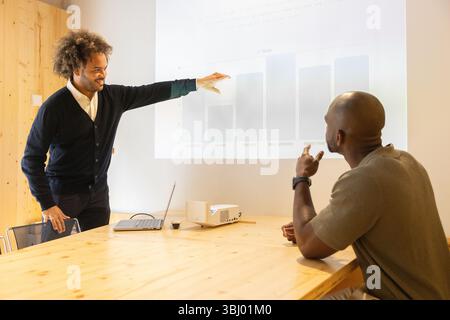 Two professionals engage in a collaborative business presentation at a modern coworking space in Barcelona, using a projector and a laptop to discuss Stock Photo