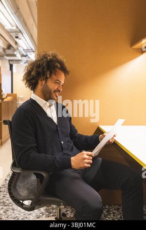 A man is seated at a desk in a modern coworking space, reviewing documents. The atmosphere is warm and professional, highlighting a collaborative work Stock Photo