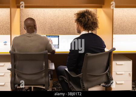 Two professionals collaborate in a modern coworking space in Barcelona, working on a laptop in a vibrant shared office setting, fostering creativity a Stock Photo