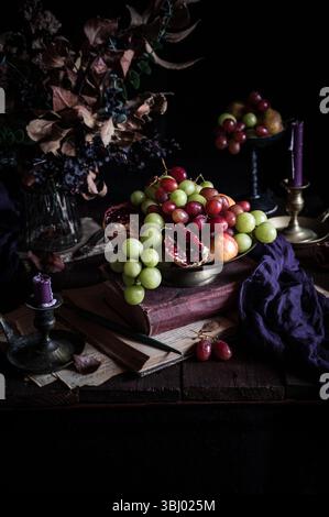 A rustic still life featuring green and red grapes, pomegranates, and apples artfully arranged in a ceramic bowl on a wooden table adorned with vintag Stock Photo