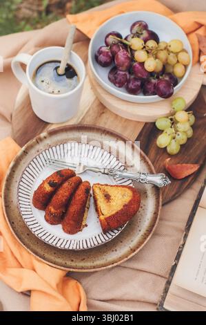 A slice of pumpkin cake is artfully plated with a fork on a rustic dish, accompanied by a cup of coffee and a bowl of grapes, creating a cozy autumn s Stock Photo