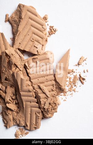 A close up view of crushed makeup products, showcasing beige face powder textures on a white background, highlighting the intricate details for beauty Stock Photo