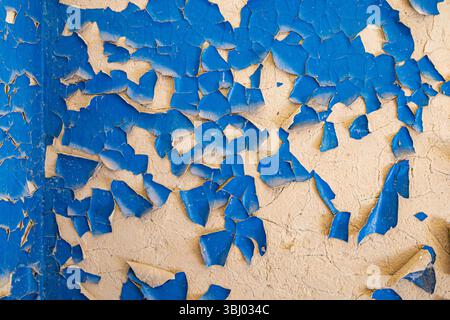 Close-up of blue peeling paint on a beige wall with cracks. Grunge surface texture for design, background, or construction themes. Stock Photo