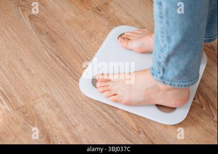 Young woman standing barefoot on digital scales at home, focusing on healthy lifestyle and monitoring weight. Concept of fitness, self-care, and weigh Stock Photo