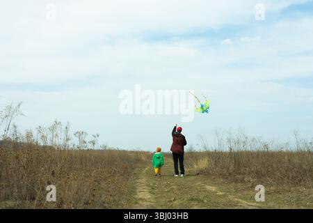 A joyful scene of a father and son flying a colorful kite in an open field. The clear sky and expansive landscape create a perfect setting for this he Stock Photo