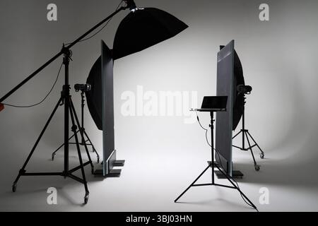 A well-equipped photography studio featuring professional lighting equipment, including softboxes and reflectors, set against a minimalist white backd Stock Photo