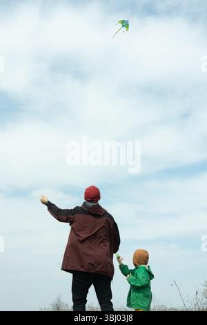 A father and son bond over kite flying in a vast open field. The dad helps his son fly the colorful kite under a clear blue sky, creating joyful famil Stock Photo