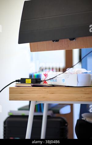 View of an opened white tissue box on a bamboo colored desk with white feet, near black charger for the screen laptop Stock Photo
