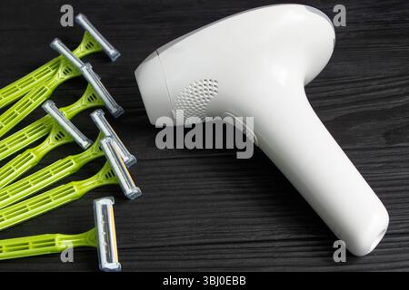 home modern laser epilator and disposable razors. Hair Remover offering Permanently Smooth Skin. Flash Epilator Laser on a black wooden background. Fe Stock Photo