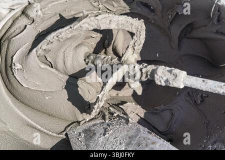 Sun shines to wet mortar cement paste mixed in bucket, closeup detail from above Stock Photo