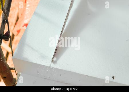 Construction worker cutting polystyrene foam heat insulation with hand saw, closeup detail from above Stock Photo