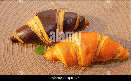Two fresh croissants, one classic golden and the other dark chocolate, lie on a decorative woven mat. Ideal for breakfast or dessert in a cozy setting Stock Photo