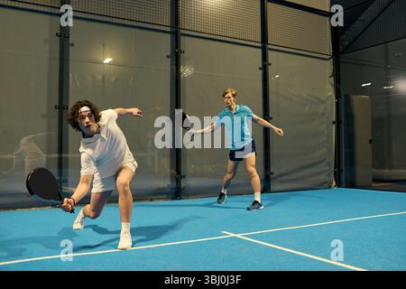 Two young sportsmen showcase their skills playing padel in an indoor arena. Stock Photo