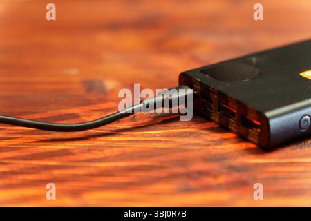 A user plugs a USB cable into a power bank on a wooden surface. The device features multiple ports Stock Photo
