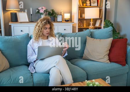 Young woman at home holding credit card and using laptop for online shopping, financial planning, booking travel, or checking banking account, relaxed Stock Photo