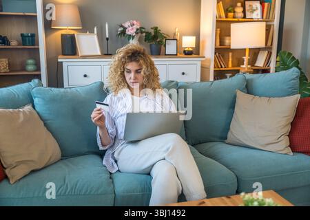 Young woman at home holding credit card and using laptop for online shopping, financial planning, booking travel, or checking banking account, relaxed Stock Photo