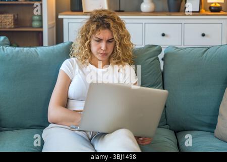 Young woman working from home on laptop experiencing technical issues such as internet disconnection, computer glitch or system error, frustrated and Stock Photo