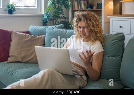 Young woman working from home on laptop experiencing technical issues such as internet disconnection, computer glitch or system error, frustrated and Stock Photo
