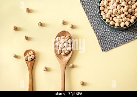 Two wooden spoons filled with dried chickpeas on yellow background. Minimalist kitchen scene with natural tones and healthy lifestyle concept Stock Photo