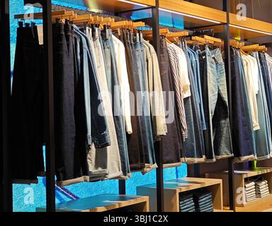 Guangzhou, China - June 8th 2025: different clothes on hangers for sale under bright light in the shopping mall Stock Photo