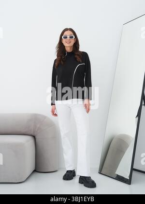 Striking brunette model showcases modern fashion in a stylish studio setting Stock Photo