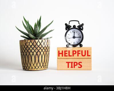 Helpful tips symbol. Wooden blocks with words Helpful tips. Beautiful white background with alarm clock and succulent plant. Business and Helpful tips Stock Photo