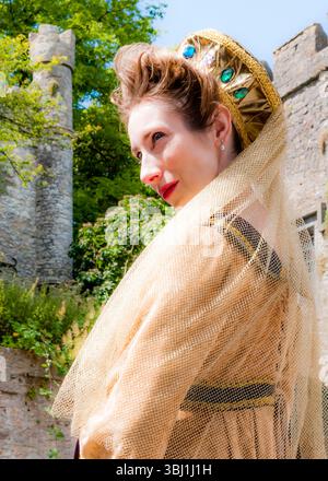 A woman in historical costume, possibly a queen or noblewoman, poses outdoors. She wears a gold headdress with jewels and a veil, and is set against a Stock Photo