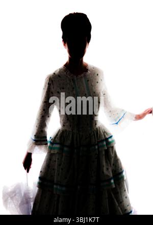 A silhouetted woman in a vintage dress holds an umbrella. Stock Photo