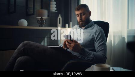 Focused Professional Stock Exchange Trader Using Smartphone, Analyzing Real-Time Stocks and Exchange Market Charts. Successful Investment Agent Working in Cozy Office of Financial Agency. Stock Photo