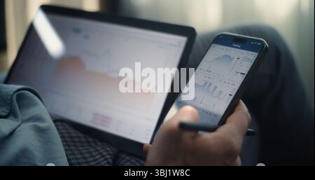 Close Up of Successful Businessman Working on Smartphone and Tablet Computer Displaying Real-Time Stocks and Exchange Market Charts in Online Trading App. Professional Financial Expert in Office. Stock Photo