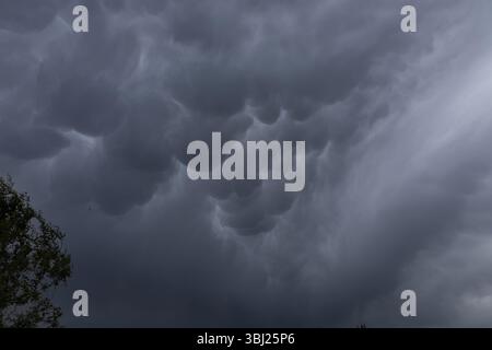 Ominous mammatus clouds form in the sky, signaling an approaching storm. The unusual pouch-like structures and dark gray tones create a powerful and e Stock Photo