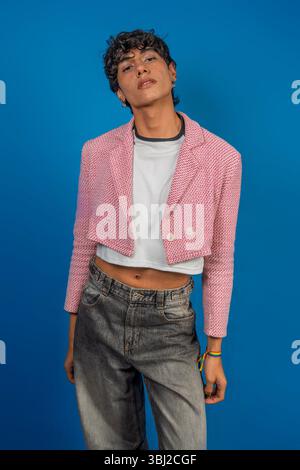 Fashionable young latin model wearing pink jacket, white t-shirt and jeans, posing with lgbt bracelet on blue background Stock Photo