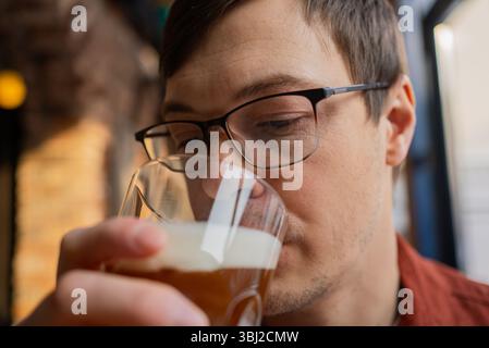 Brewer enjoying the aroma of craft beer in a glass at a brewery or bar, savoring a fresh recipe while engaging in quality control for the perfect brew experience Stock Photo