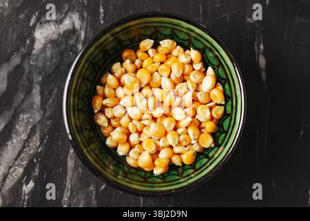 Dry corn kernels in green bowl. Organic grains on dark marble table. Natural food ingredient. Rustic kitchen concept. Yellow textured seeds. Stock Photo