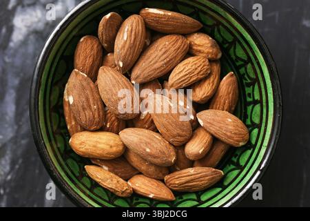 Raw almonds in green bowl. Healthy organic nuts on dark marble. Crunchy vegetarian snack. Natural food source of protein and fiber. Stock Photo