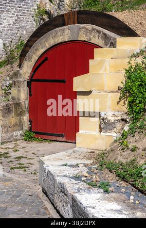 A vibrant red wooden door set in a stone archway, surrounded by greenery and a cobblestone path. The door is slightly ajar, inviting curiosity. Stock Photo