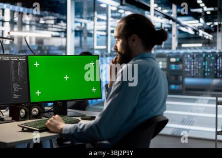 Technician using green screen mockup PC in data center to update servers tech, configuring equipment using software tools. Server room employee reviewing hardware analytics on chroma key PC Stock Photo