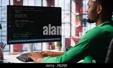 Male programmer types code on computer and running script, programming language. African american IT expert in modern loft fixing errors within the software, implementing new features. Camera A. Stock Photo