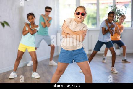 Girl in stylish glasses and clothes dances hip hop and other modern dances in studio with friends Stock Photo